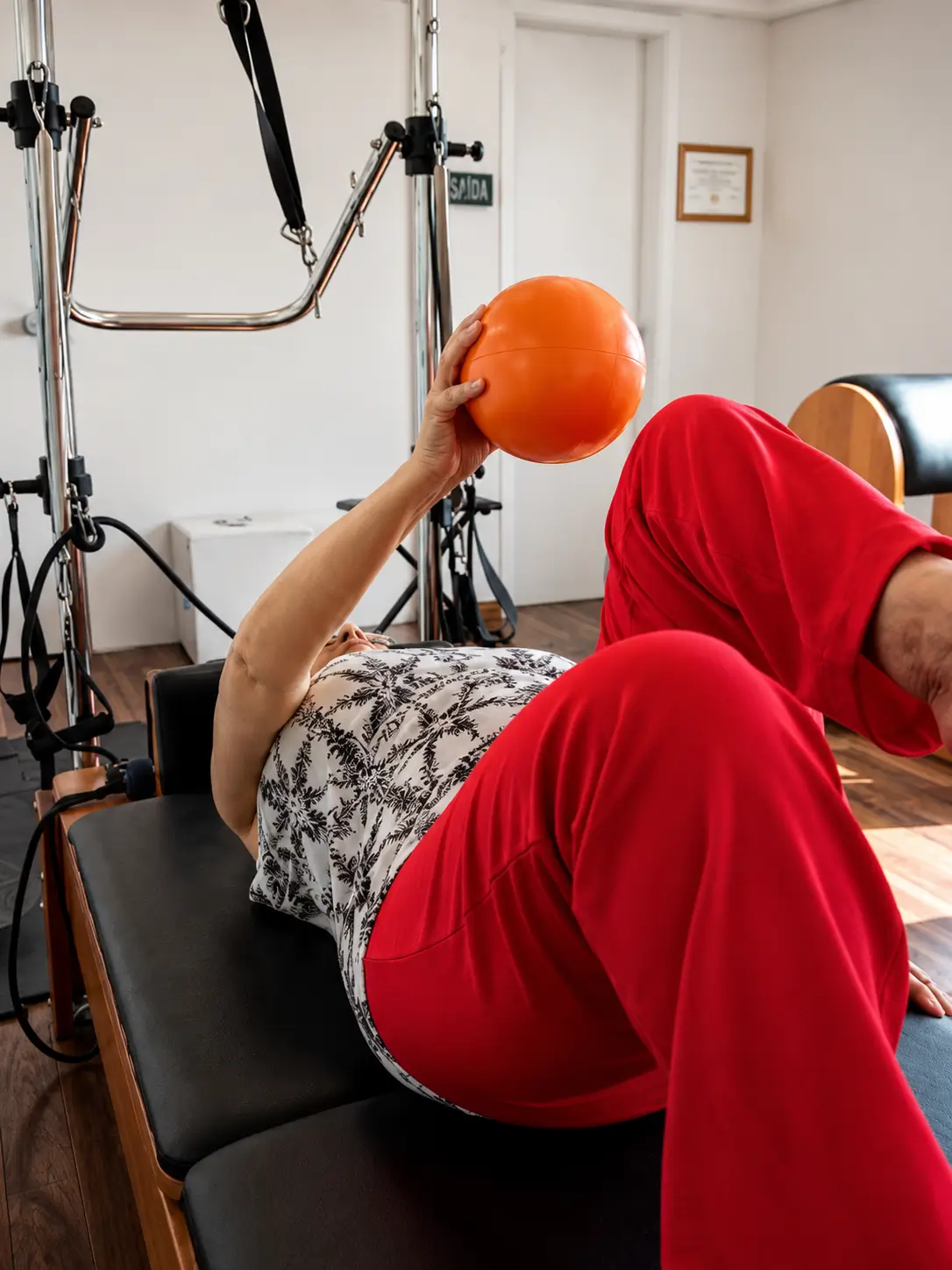 Paciente em exercício de fortalecimento com bola durante atendimento de fisioterapia com equipamento de Pilates